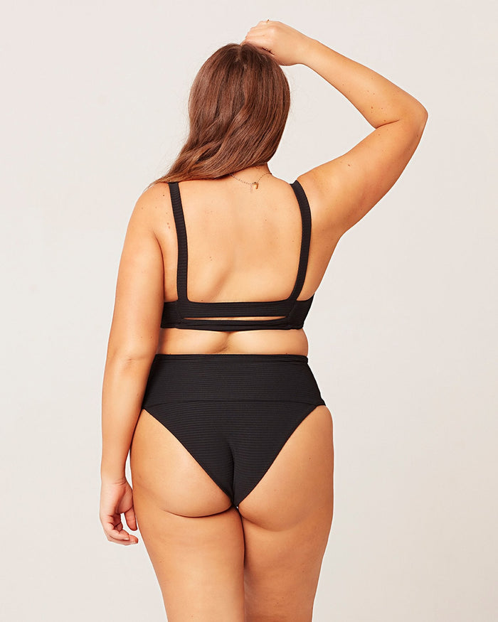 Back view of a model wearing the LSPACE black Jess Bikini Top, showing the cross-back strap detail, paired with the black Desi Bikini Bottom.