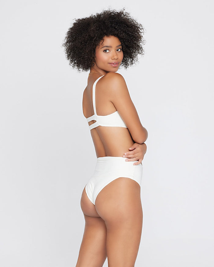 Back view of a model wearing the LSPACE cream Jess Bikini Top, showing the strap detail at the back, paired with the matching cream Desi Bikini Bottom.