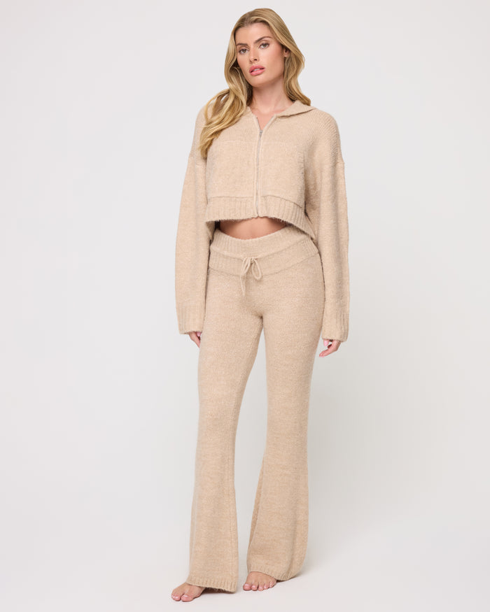Full-length front view of a model wearing the LSPACE Jet Set Pant - Heather Oatmeal in heather oatmeal, a flared knit pant with a drawstring waistband and cozy texture, styled with a matching cropped zip-up hoodie.