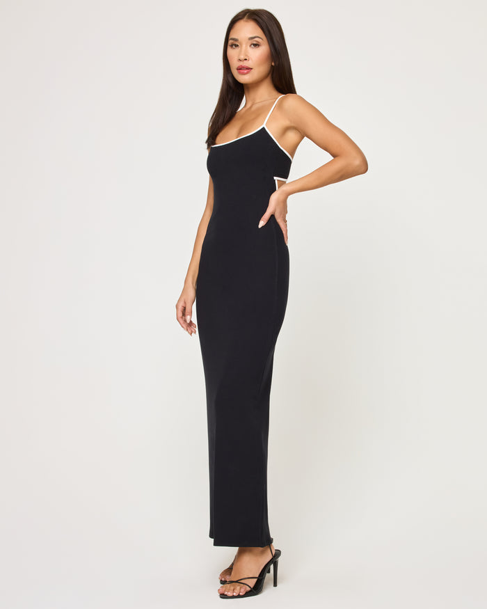 Full-length side view of a model wearing the LSPACE Jordana Dress in black-cream, showing the fitted silhouette with cream contrast trim on the spaghetti straps.