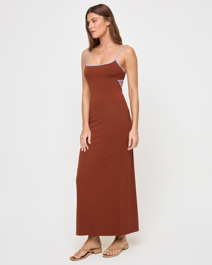 Side view of a model wearing the LSPACE Jordana Dress in tobacco peri blue, showing the fitted silhouette with periwinkle blue contrast trim and a glimpse of the open-back detail.