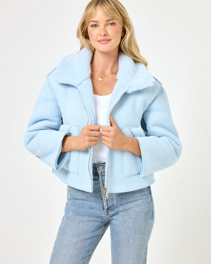 Close-up front view of a model wearing the LSPACE Kalina Jacket in ice blue, detailing the plush sherpa collar, zip-front closure, and cropped boxy silhouette of the reversible jacket.