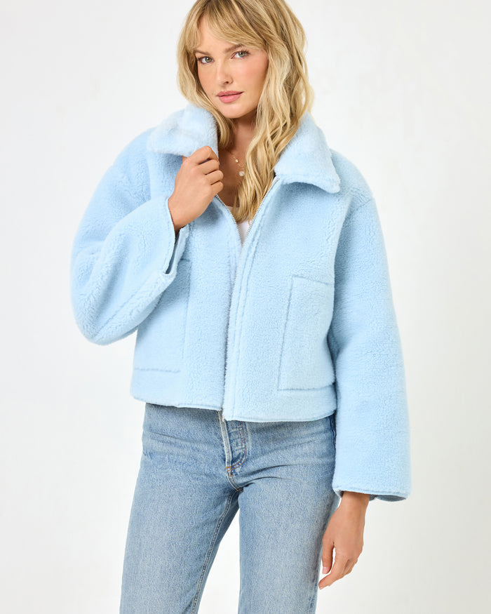 Front view of a model wearing the LSPACE Kalina Jacket in ice blue, showing the fluffy sherpa exterior, wide lapel collar, front zip closure, and patch pockets of the cropped jacket.
