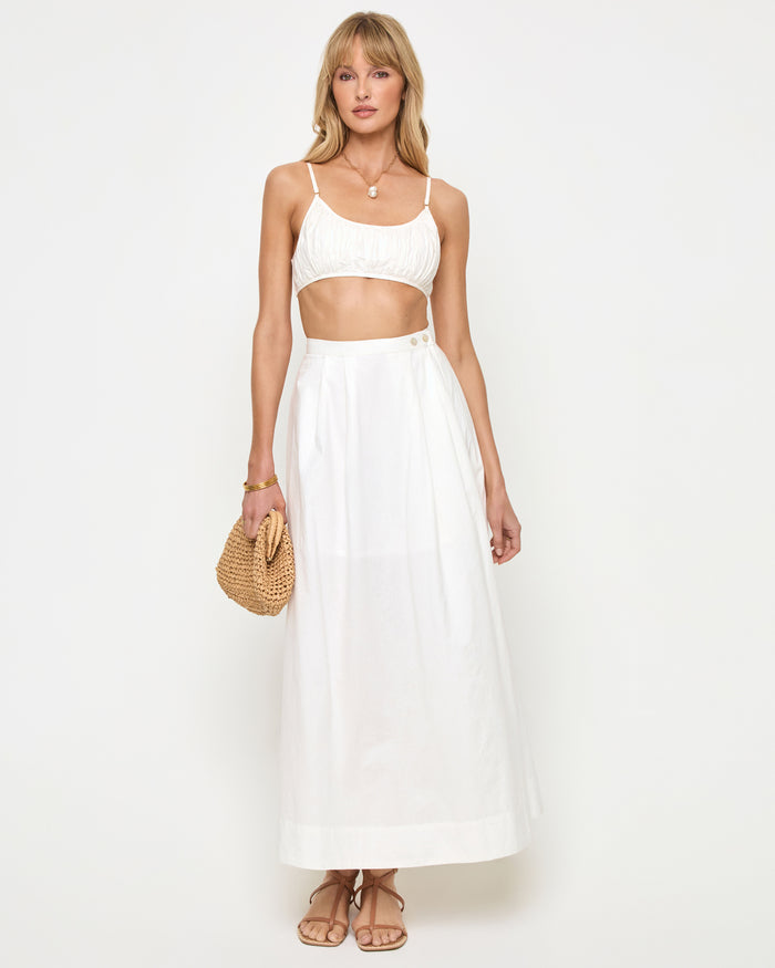 Front view of a model wearing the LSPACE Keeper Skirt in white, a high-waisted maxi skirt with button detail at the hip and A-line silhouette, styled with a white crop top.