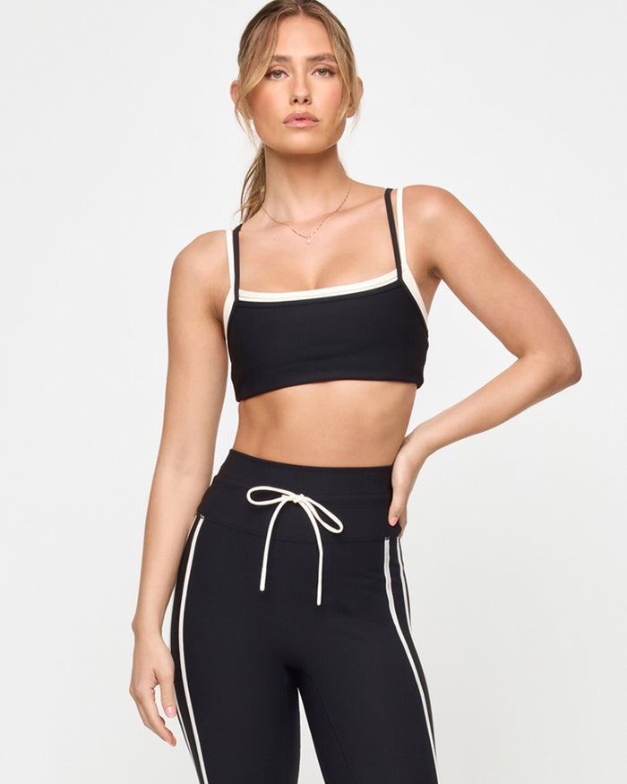 Front view of the LSPACE Kelly Bra in black-cream on a model against a light background, showing the sports bra design with cream trim detail, paired with black-cream high-rise active pants.