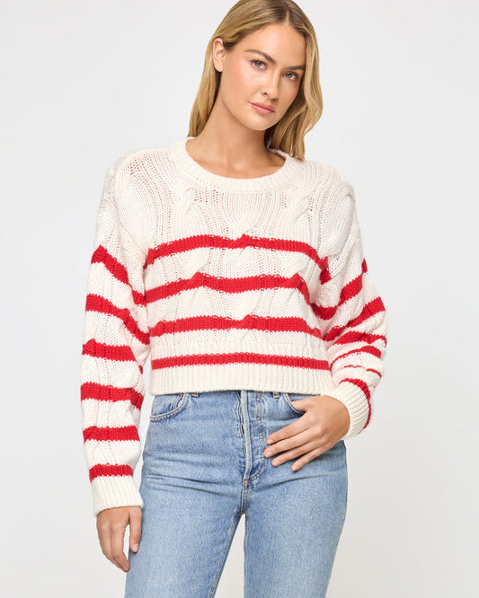 Front view of a model wearing the LSPACE Kensley Pullover in cream flame, a cropped cable-knit sweater with red horizontal stripe detailing, crew neckline, and long sleeves.