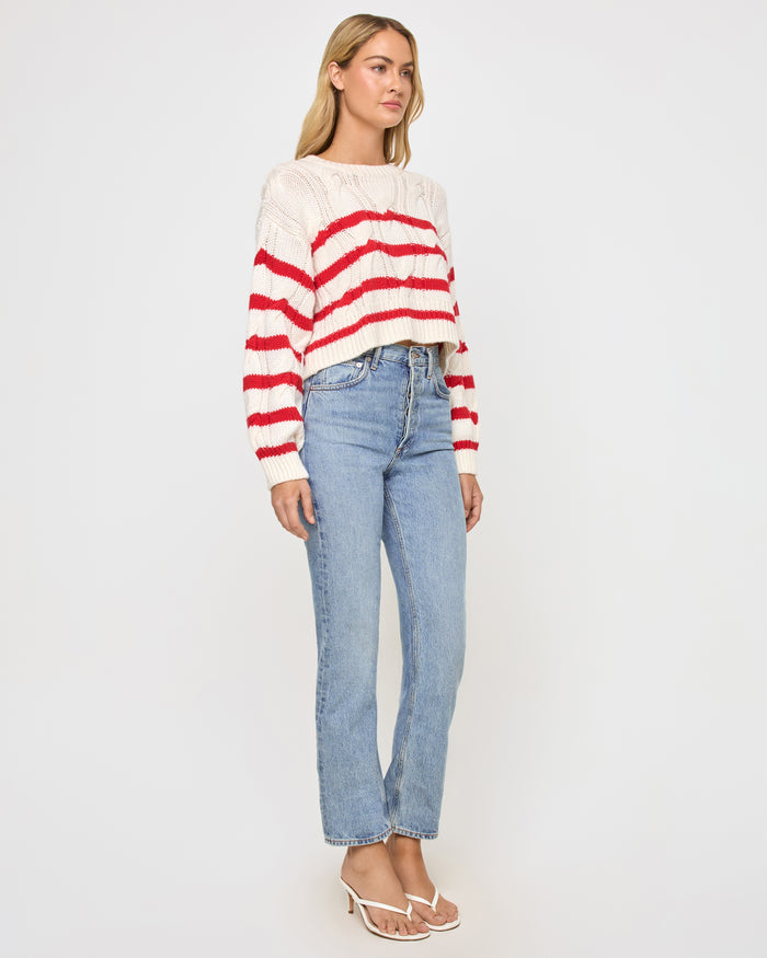 Side view of a model wearing the LSPACE Kensley Pullover in cream flame, showing the cropped cable-knit silhouette with red horizontal stripes and relaxed fit.