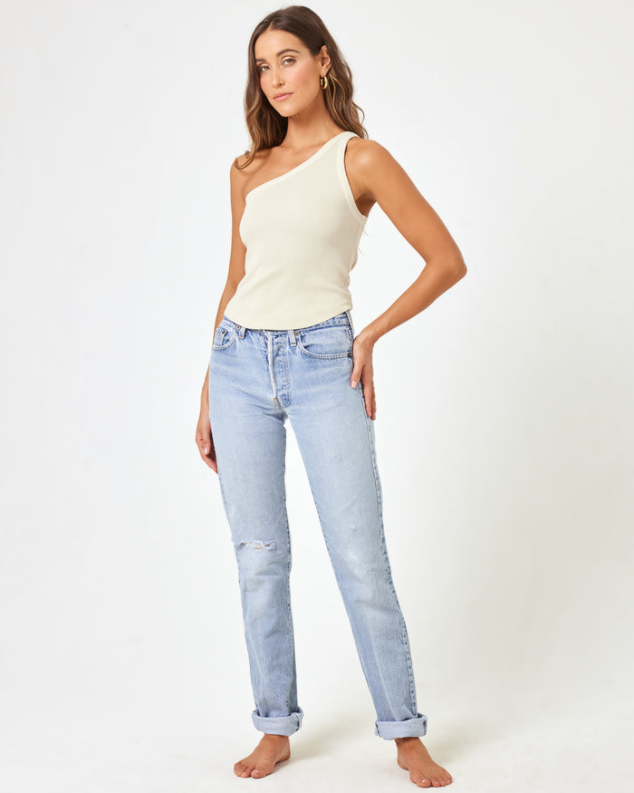 Front view of a model wearing the LSPACE Kylie Tank in bone, an off-white ribbed one-shoulder crop tank, paired with light wash distressed straight-leg jeans.