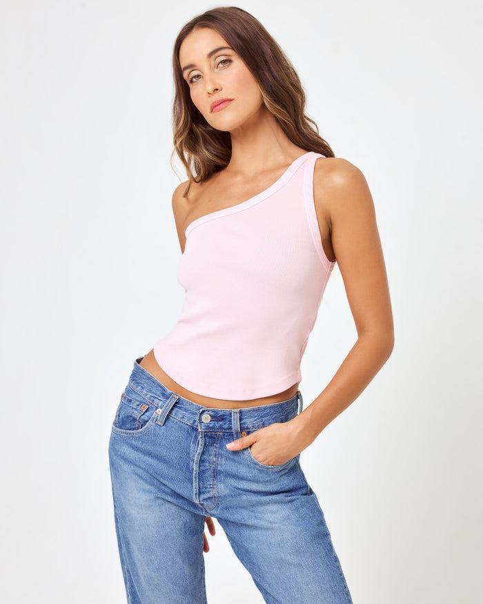 Three-quarter front close-up of a model wearing the LSPACE Kylie Tank in petal, a blush pink ribbed one-shoulder crop tank, paired with medium wash blue jeans.