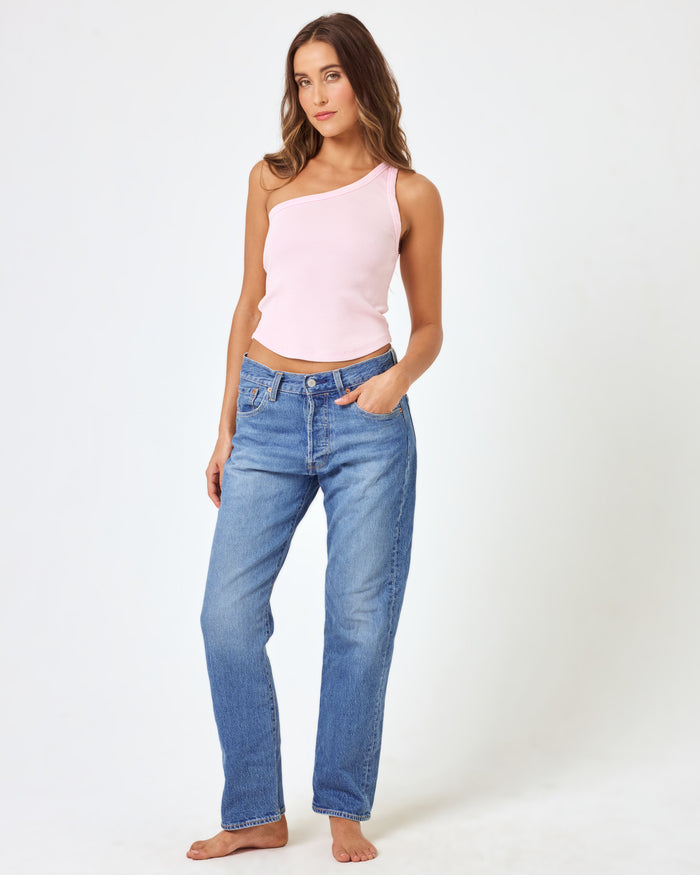 Front view of a model wearing the LSPACE Kylie Tank in petal, a blush pink ribbed one-shoulder crop tank with an asymmetric neckline, paired with medium wash jeans.