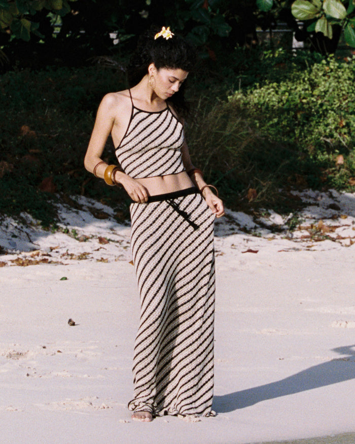 Front view of a model wearing the LSPACE La Bianca Skirt in tip the scales stripe, a maxi-length crochet skirt with diagonal black and cream stripes and a black tie waistband.
