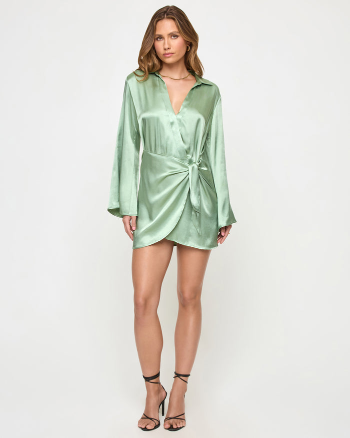Front view of a model wearing the LSPACE Las Palmas Dress in celadon, a satin mini shirt dress with a collar, long sleeves, deep V-neckline, and a knotted tie at the waist.