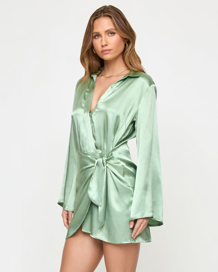 Three-quarter front view of a model wearing the LSPACE Las Palmas Dress in celadon, highlighting the knotted front waist tie and satin fabric sheen.