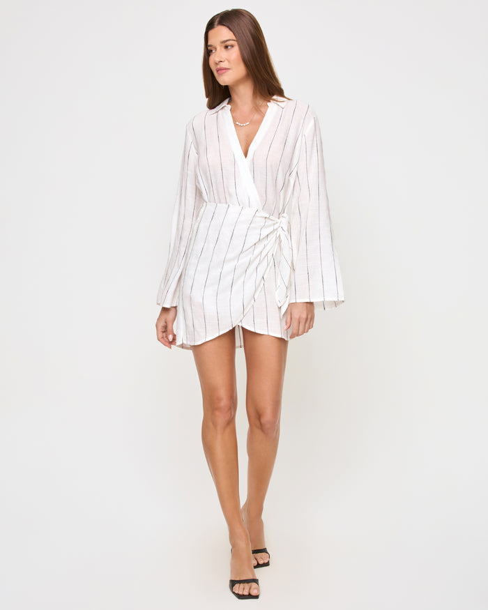 Full-length front view of a model wearing the LSPACE Las Palmas Dress in fine line stripe, showing the short wrap mini silhouette with fine vertical stripes, long flared sleeves, and a tie waist closure.