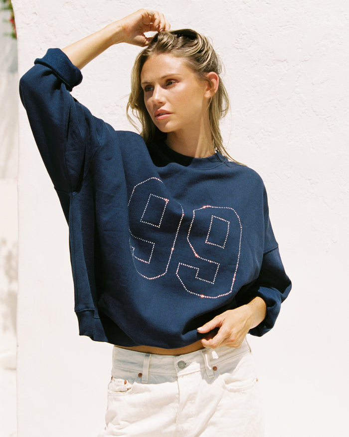 Front view of a model wearing the LSPACE Legend Sweatshirt in midnight blue, a cropped navy sweatshirt featuring a rhinestone studded '99' graphic on the front.