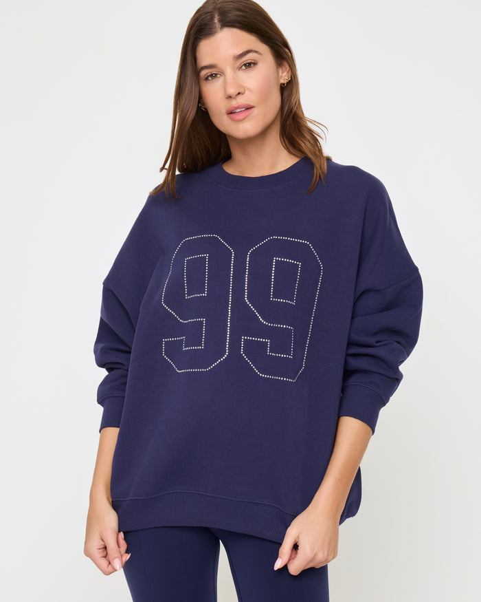 Front view of a model wearing the LSPACE Legend Sweatshirt in midnight blue, an oversized crew-neck sweatshirt with a rhinestone studded '99' graphic.