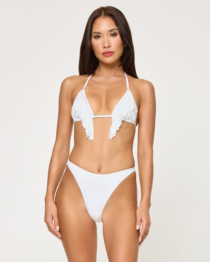Front view of a model wearing the LSPACE white Leilani Bikini Bottom with a high-cut leg, paired with a white fringe halter bikini top.