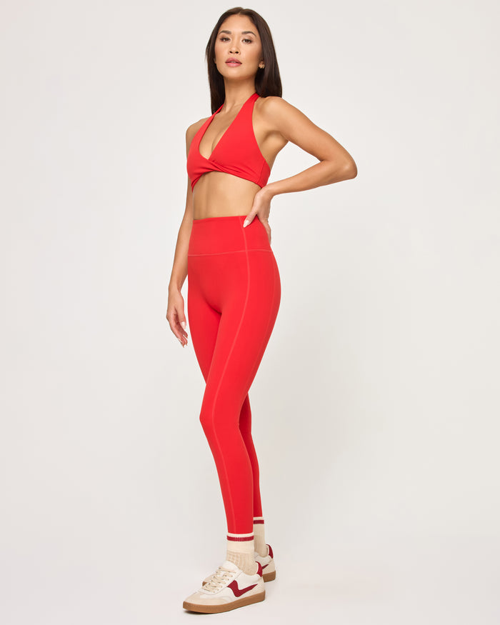 Side view of model wearing the Level Up Legging in flame with matching flame Jeanne Bra, striped socks and sneakers.
