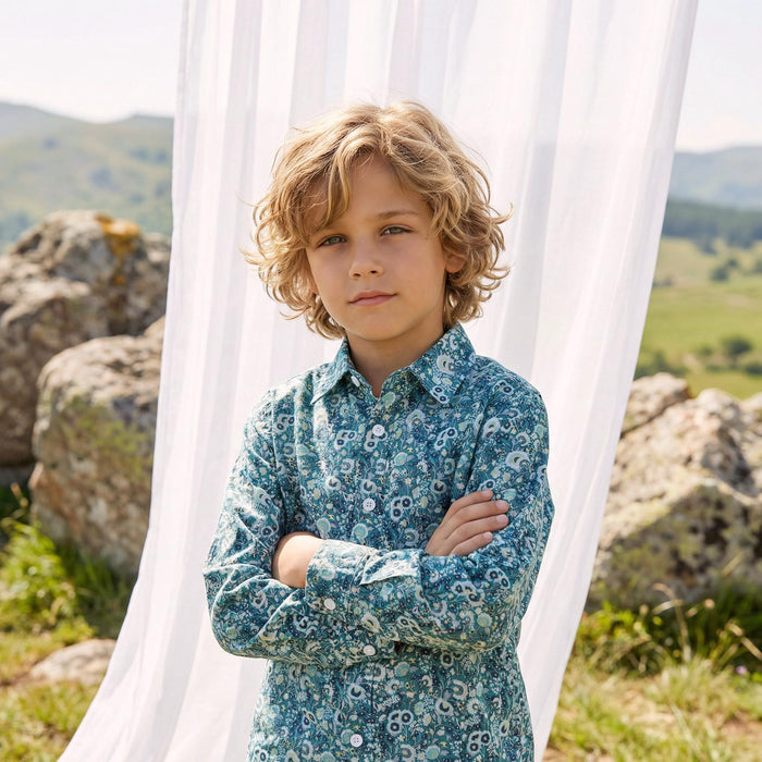 May include: A teal button-down shirt with a white floral pattern. The shirt has long sleeves and a classic collar. The shirt is worn by a person with blonde curly hair, standing outdoors with arms crossed.