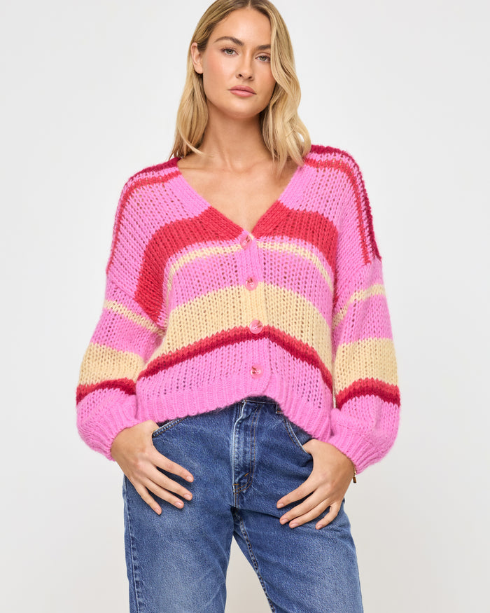 Front view of a model wearing the LSPACE Lido Cardigan in catch some rays, a colorful striped open-knit cardigan with broad horizontal stripes in pink, red, and cream, featuring a v-neckline and button-front closure.