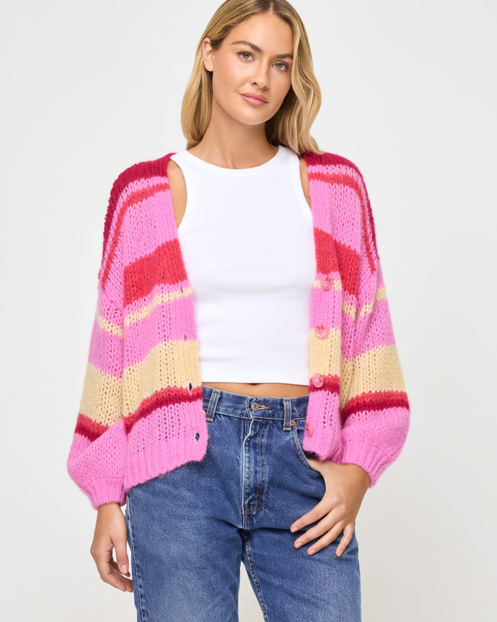 Front view of a model wearing the LSPACE Lido Cardigan in catch some rays unbuttoned, showing the colorful horizontal stripe knit pattern in pink, red, and cream with button-front closure and billowy sleeves.