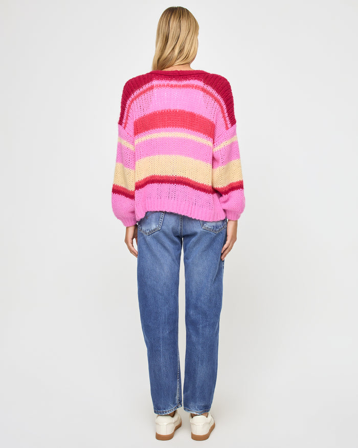 Back view of a model wearing the LSPACE Lido Cardigan in catch some rays, showing the horizontal stripe pattern in pink, red, and cream across the back of the open-knit cardigan.