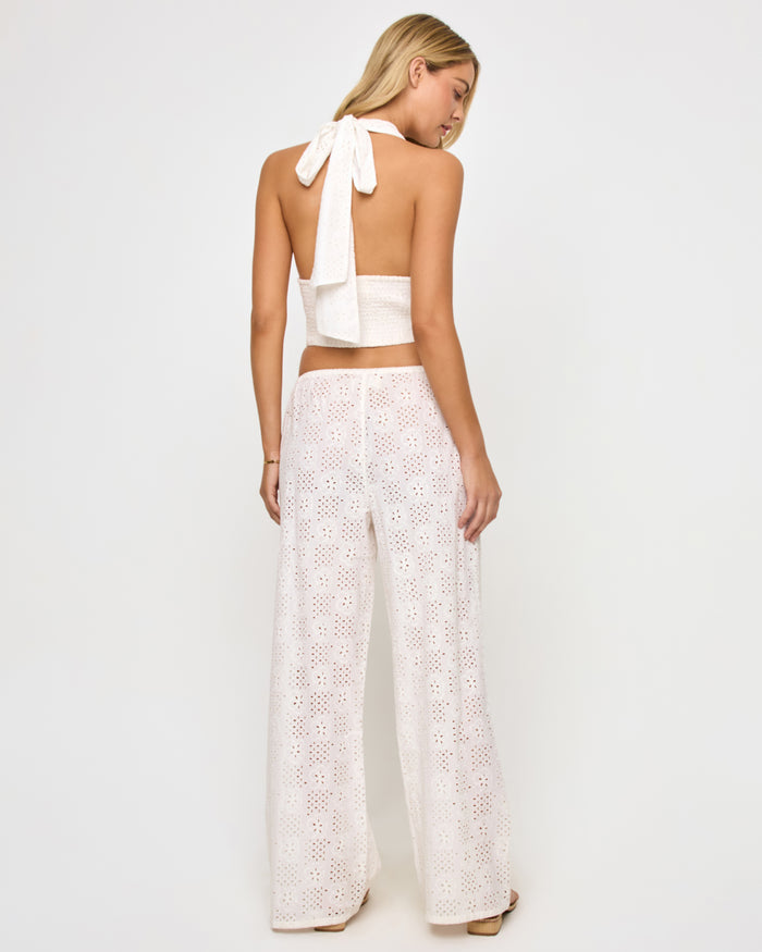 Back view of a model wearing the LSPACE Lily Pant in cream, showing the full-length back of the wide-leg eyelet pants with the geometric floral broderie anglaise pattern, styled with the matching halter top.