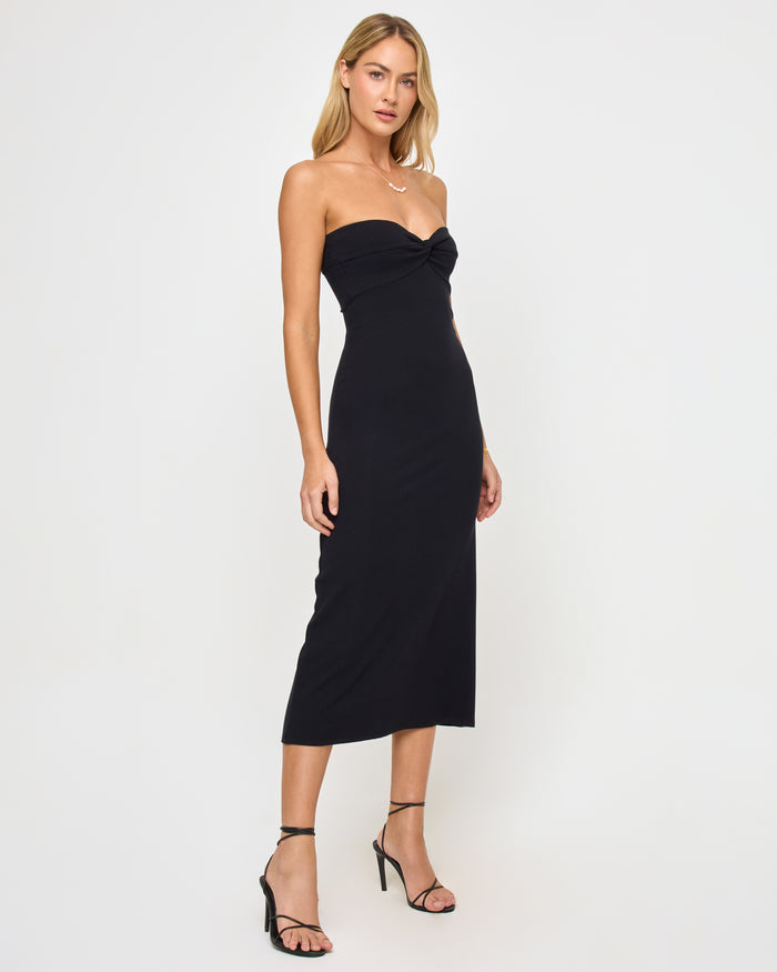 Three-quarter front view of a model wearing the LSPACE Lisette Dress in black, showing the body-conscious midi silhouette and twisted sweetheart neckline.