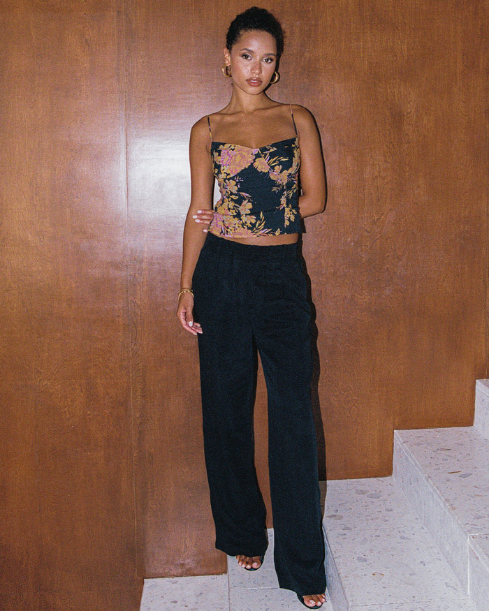 Front full-length view of a model wearing the LSPACE Lottie Top in through thick and thorns, featuring a dark floral corset-style crop top with spaghetti straps, styled with black wide-leg pants.
