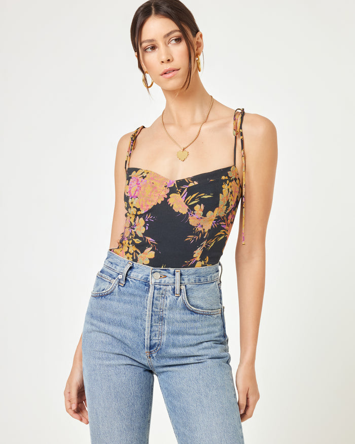 Front three-quarter view of a model wearing the LSPACE Lottie Top in through thick and thorns, showing the dark floral corset crop top with spaghetti straps, styled with blue jeans.