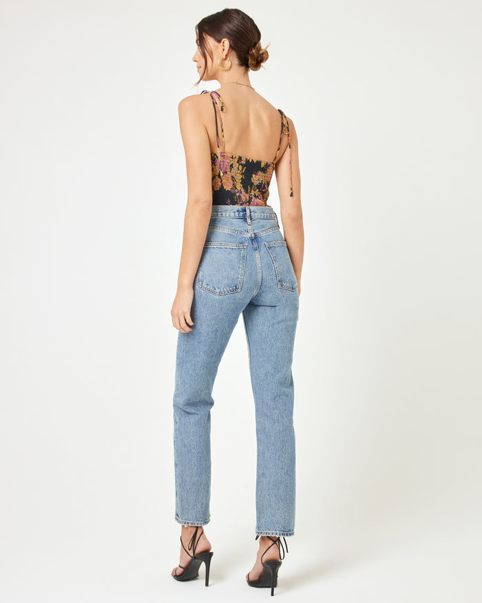 Back full-length view of a model wearing the LSPACE Lottie Top in through thick and thorns, showing the open back with tie straps of the dark floral corset crop top, paired with blue jeans and strappy heels.