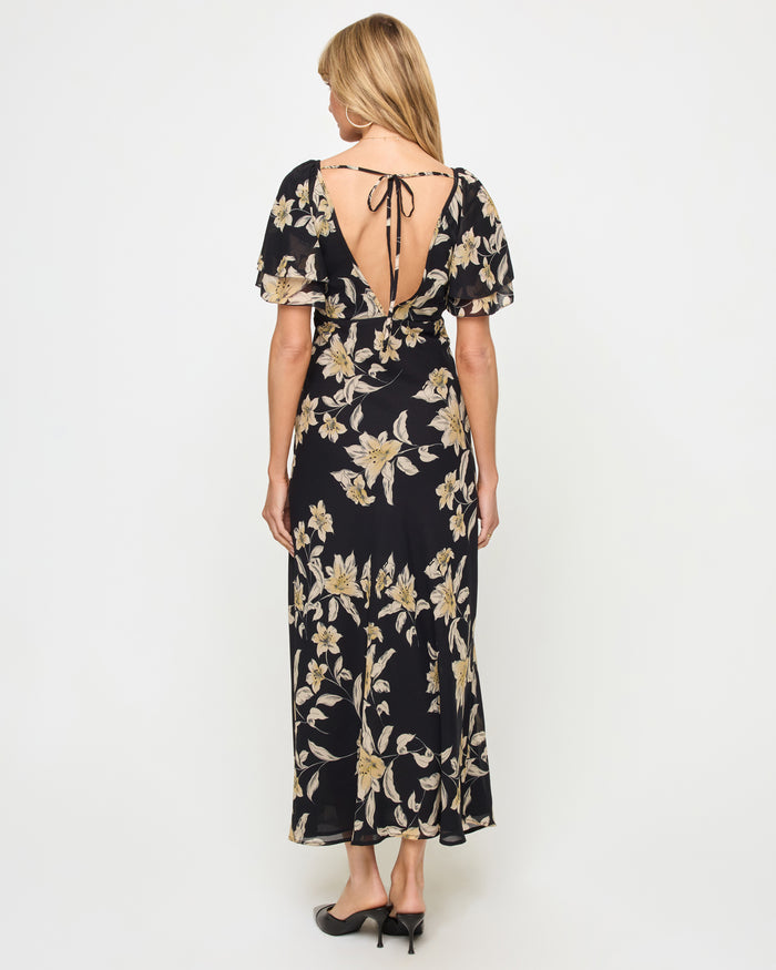 Back view of a model wearing the LSPACE Lover Maxi Dress in petal to the metal, showing an open back with a tie closure and a flowing full-length silhouette.