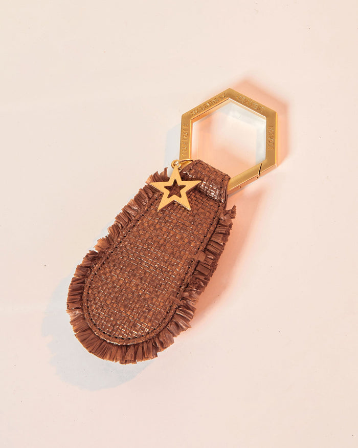 Off-model image of the LSPACE x Lindsay Albanese TOPTOTE in tobacco showing the woven raffia body with fringe trim, gold hexagonal carabiner ring, and star charm.