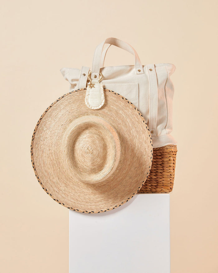 Off-model image of the LSPACE x Lindsay Albanese TOPTOTE in a natural colorway clipped to a canvas tote bag alongside a straw hat on a white pedestal.