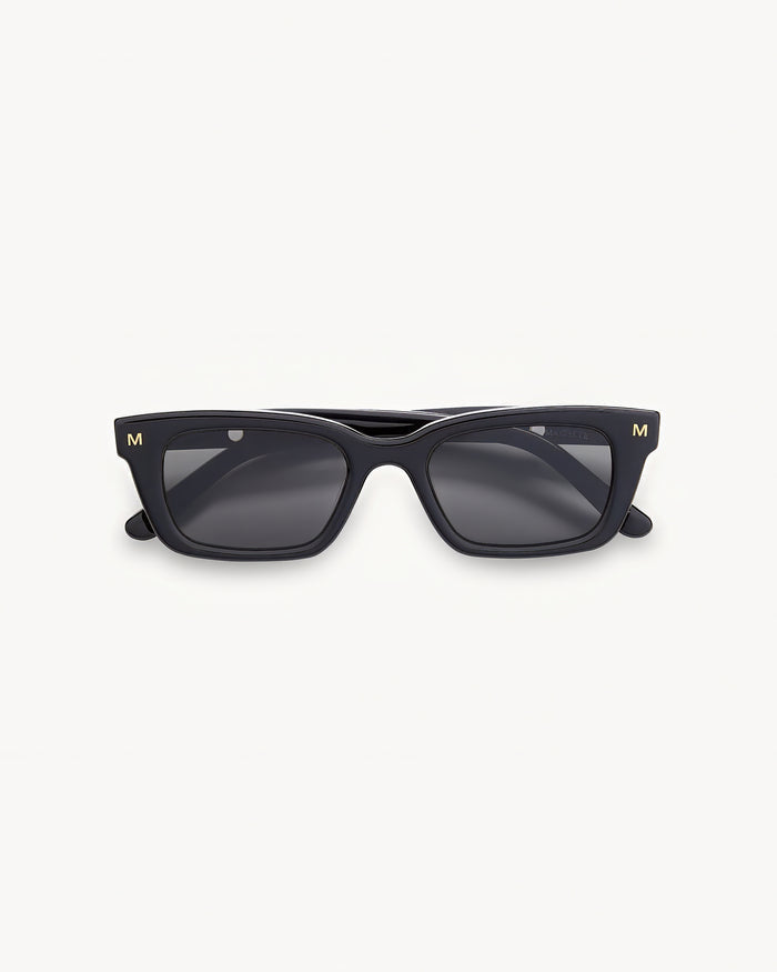 Off-model image of the Machete Ruby Sunglasses in black, folded flat with a black acetate rectangular frame and dark grey lenses.