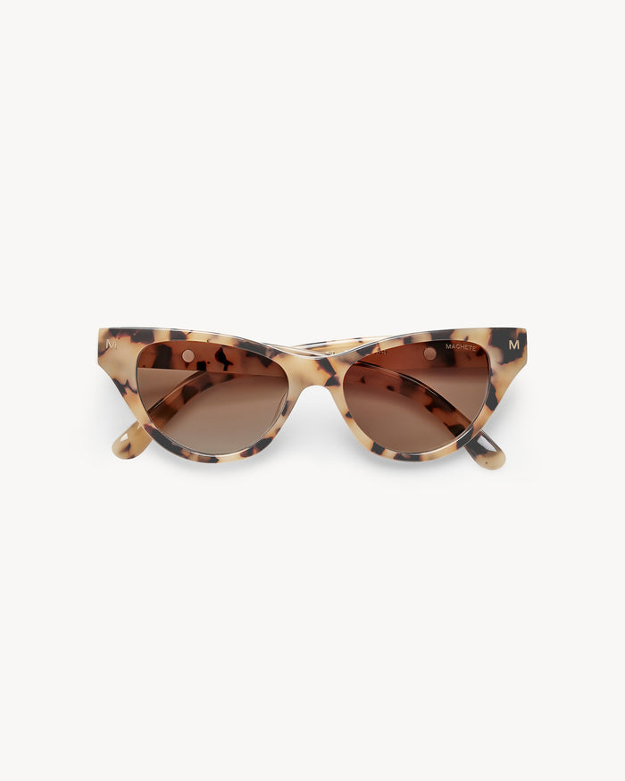 Off-model image of the Machete Suzy Sunglasses in blonde tortoise, folded flat with cat-eye blonde tortoise acetate frame and brown gradient lenses.