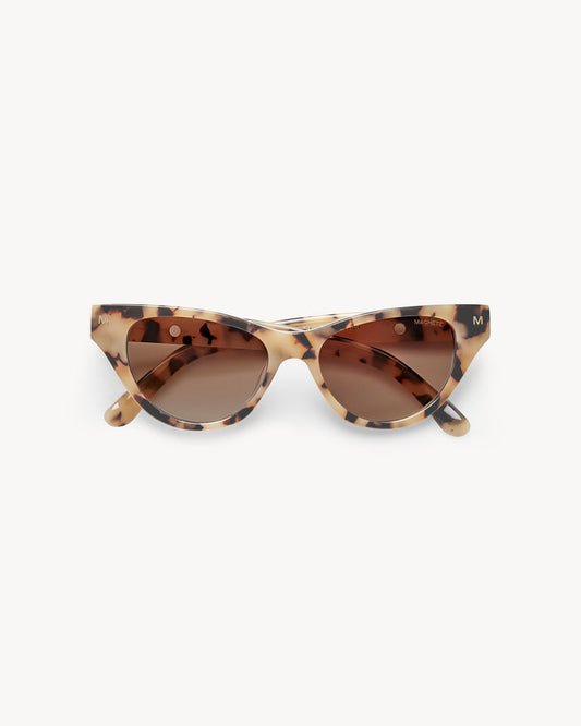 Off-model image of the Machete Suzy Sunglasses in blonde tortoise, folded flat with cat-eye blonde tortoise acetate frame and brown gradient lenses.