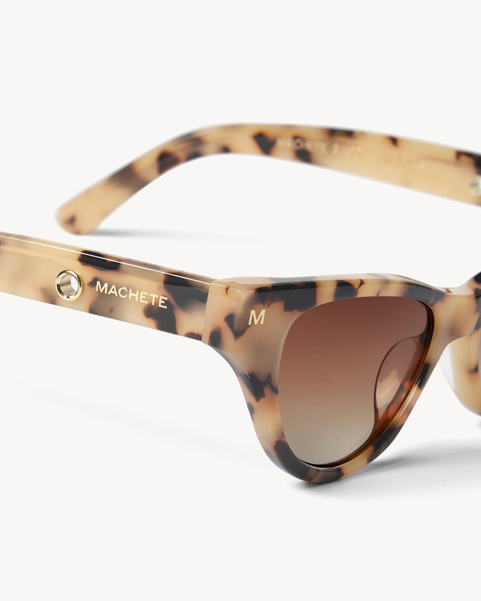 Close-up detail of the Machete Suzy Sunglasses in blonde tortoise showing the Machete branding on the temple arm and the brown gradient lenses.