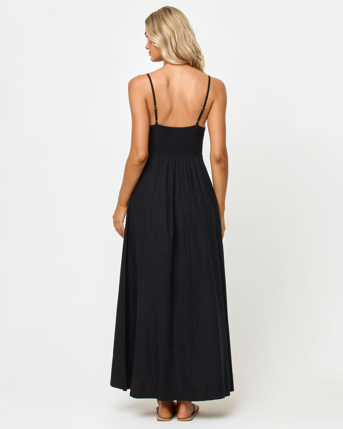 Back view of a model wearing the LSPACE Mallorca Dress in black, showing the adjustable spaghetti straps and smocked back bodice of the tiered black maxi dress.