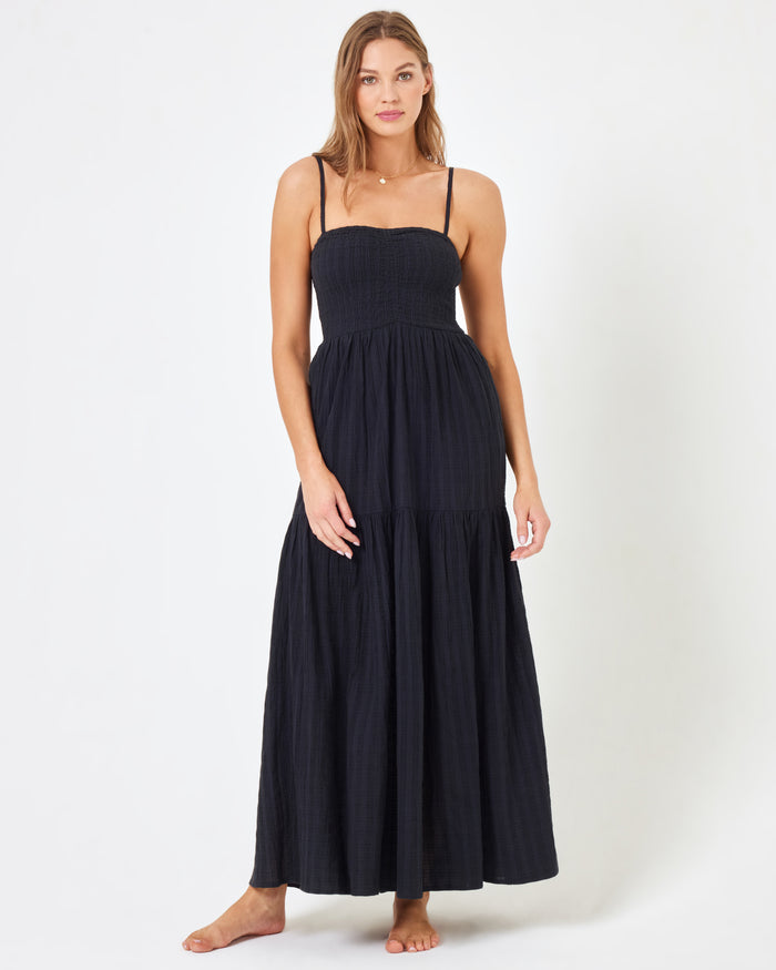 Front view of a model wearing the LSPACE Mallorca Dress in black, a smocked-bodice tiered maxi dress with spaghetti straps in a black textured fabric.