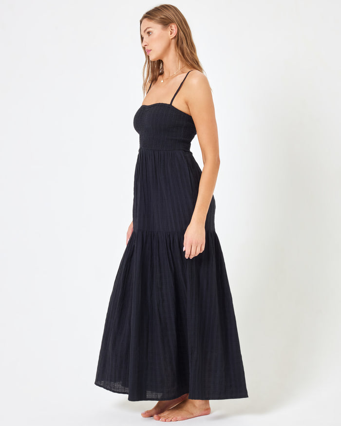 Side view of a model wearing the LSPACE Mallorca Dress in black, showing the tiered maxi skirt and smocked bodice silhouette.