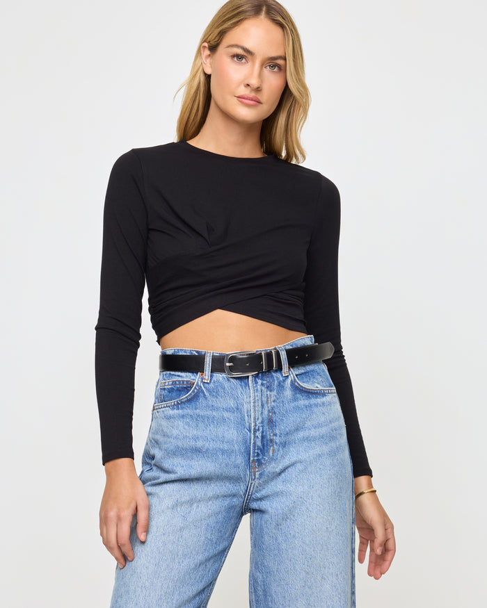 Front view of a model wearing the LSPACE Marseille Top in black, a long-sleeve cropped top with a crew neckline and a twisted crossover hem detail.