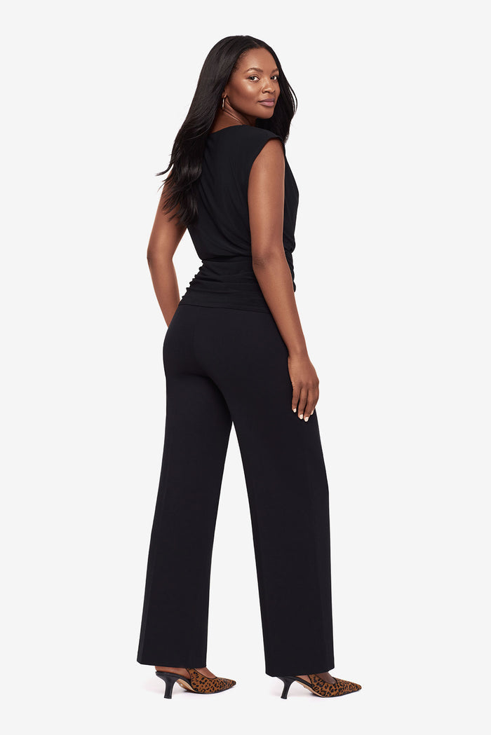 Woman in a black high neck blouse with matching wide leg pants turned left