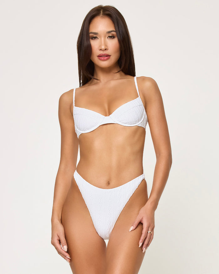 Front view of a model wearing the LSPACE Eyelet White Missy Bikini Top, a structured underwire style with thin adjustable straps in textured eyelet fabric, paired with matching white eyelet high-cut bikini bottoms.