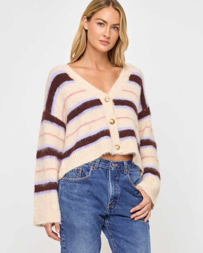 Front view of a model wearing the LSPACE Montauk Cardigan in prep school stripe, a cropped oversized V-neck button-front cardigan in a soft eyelash knit with horizontal stripes in cream, dark brown, lavender, and pink, styled with jeans.