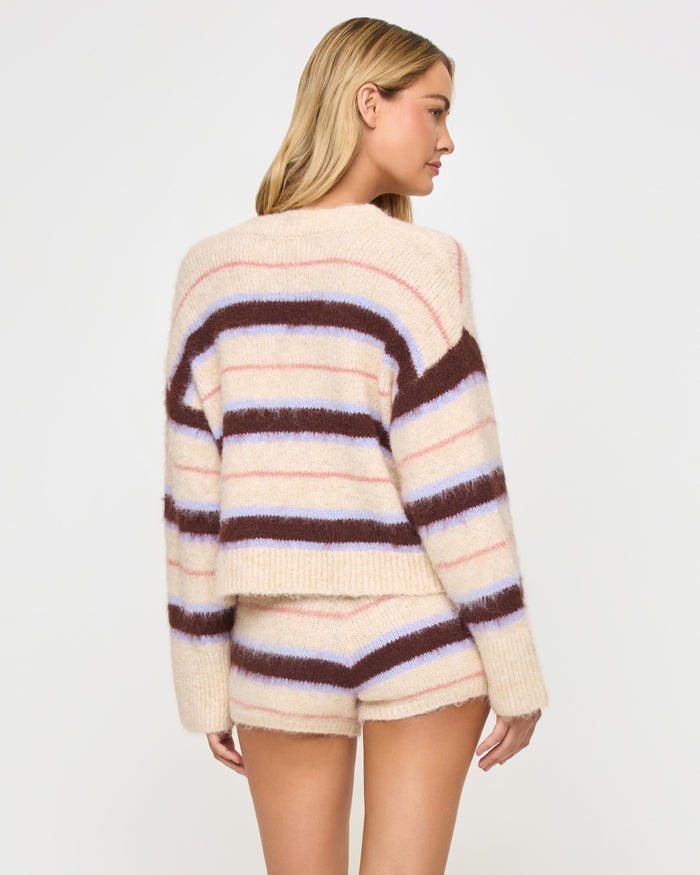 Back view of a model wearing the LSPACE Montauk Cardigan in prep school stripe, a cropped oversized button-front cardigan in a soft eyelash knit with horizontal cream, dark brown, lavender, and pink stripes, styled with the matching Montauk Short.