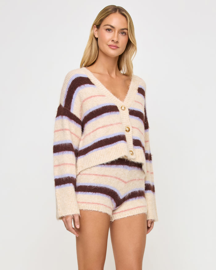 Three-quarter front view of a model wearing the LSPACE Montauk Short in prep school stripe, a mini short in a soft eyelash knit with horizontal cream, dark brown, lavender, and pink stripes, styled with the matching Montauk Cardigan.