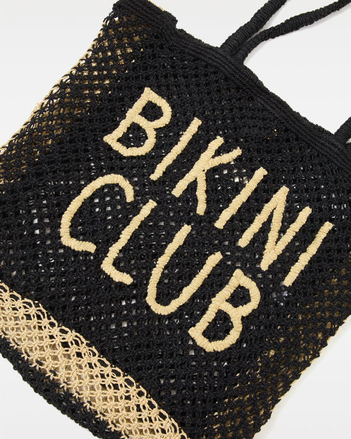 Close-up of the Moonlight Bag in natural-black showing the 'Bikini Club' intarsia lettering detail on the open-weave crochet body.