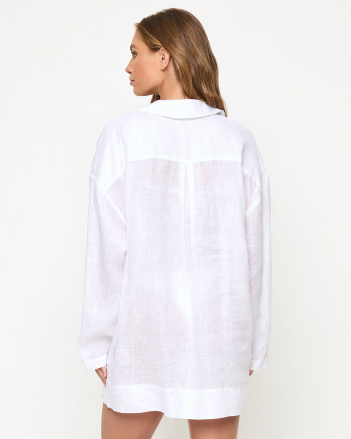 Back view of a model wearing the LSPACE Oasis Tunic in white, showing the semi-sheer linen fabric, center back seam detail, and long-sleeve cover-up silhouette.