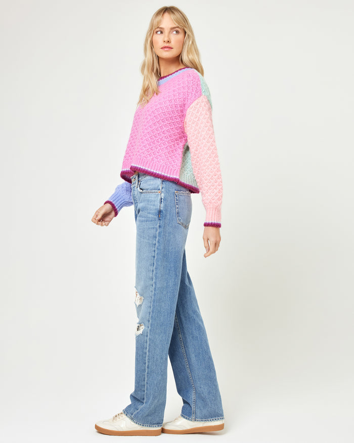 Side view of a model wearing the LSPACE Pretty Please Sweater in costa del sol colorblock, showing the chunky knit silhouette and colorblock design, paired with distressed blue jeans.